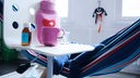 Fieberthermometer, Hustensaft, Wärmflasche und eine Tasse Tee stehen auf einem Stuhl, während ein Kind im Hintergrund in einer Hängematte liegt (Gestellte Szene)
