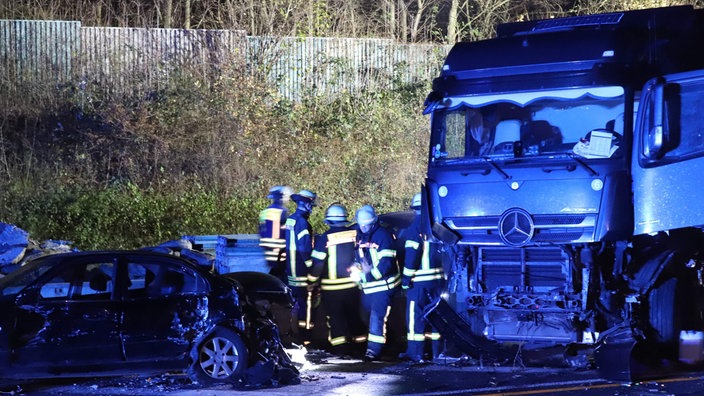 Einsatzkräfte der Feuerwehr stehen neben einem Lastwagen auf der Autobahn 1 bei Hagen an der Unfallstelle