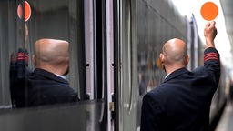 Ein Schaffner hebt am Hauptbahnhof Hannover in Hannover seine Kelle