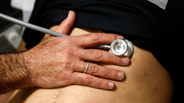 Eine Hand hält ein Stethoskop auf den Bauch eines Long-Covid-Patienten.