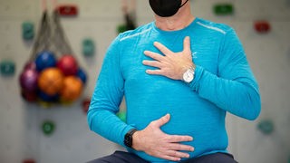 Atemtraining in einer Reha-Klinik: Ein Mann hält seine Hände auf Bauch und Brust.