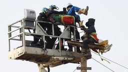 10.01.2023, Nordrhein-Westfalen, Erkelenz: Polizeibeamte entfernen einen Klimaschutzaktivisten mit Hilfe einer Hebebühne von einem Holzpfahl am Rand der Ortschaft Lützerath