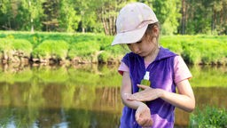Ein Mädchen steht in der Nähe eines Gewässers und benutzt Mückens-Spray, um sich vor den Insekten zu schützen.