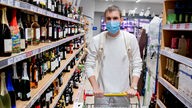 Ein junger Mann mit OP-Maske schiebt im Supermarkt einen Einkaufswagen.