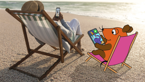 Eine Frau mit Handy in der Hand, auf dem ein Kinderfoto zu sehen ist, am Strand im Liegestuhl, neben ihr sitzt die Maus - auf ihrem Handy ist eine Nachricht an die Ente mit einem Bild des Elefanten zu sehen.