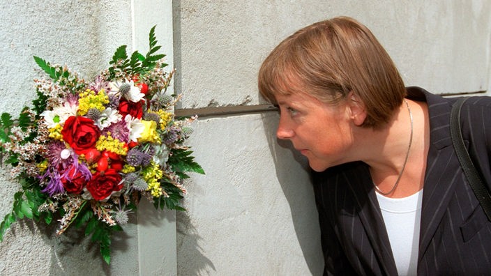 Angela Merkel (CDU) blickt am Donnerstag durch den mit einem Blumenstrauß geschmückten Sehschlitz auf den Todesstreifen der neueröffneten Gedenkstätte der Berliner Mauer im Bezirk Mitte.