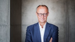 Friedrich Merz verschrenkt die Arme vor der Brust und lächelt.