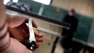 Eine Person hält in einem Klassenzimmer ein Klappmesser in der Hand.