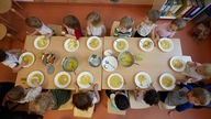 Kinder sitzen am Tisch und essen Kartoffelsuppe