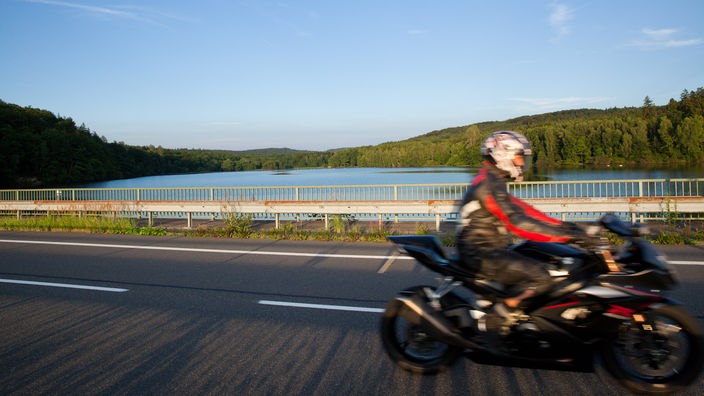 Ein Motorradfahrer fährt über den Heve-Vordamm am Möhnesee