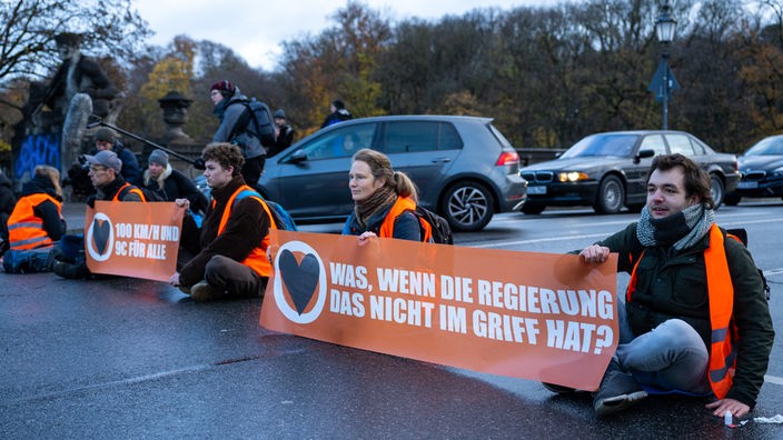 Klimaaktivisten der Umweltschutzbewegung «Letzte Generation» sitzen auf der Prinzregentenstraße und blockieren den Verkehr. Sie halten Transparente mit der Aufschrift "Was wenn die Regierung das nicht im Griff hat?"