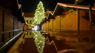 Der Weihnachtsbaum des Weihnachtsmarktes spiegelt sich auf einer regennassen Tischplatte.