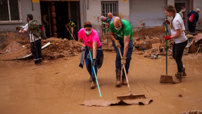 Menschen schaufeln Schlamm weg auf einer Straße in Valencia nach dem schweren Unwetter in Spanien