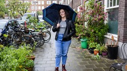 Das Bild zeigt die Journalistin Sarah Tekath, die mit einem Regenschirm in einer Straße von Amsterdam steht. 