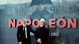 Joaquin Phoenix und Ridley Scott bei der Premiere des Kinofilms Napoleon in Madrid vor einem großen Kinoplakat