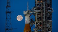 Eine Rakete steht an einer Startvorrichtung, im Hintergrund steht der Mond am Himmel