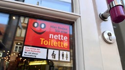 An der Eingangstür eines Cafés hängt ein Schild mit der Aufschrift "Hier finden Sie eine nette Toilette"