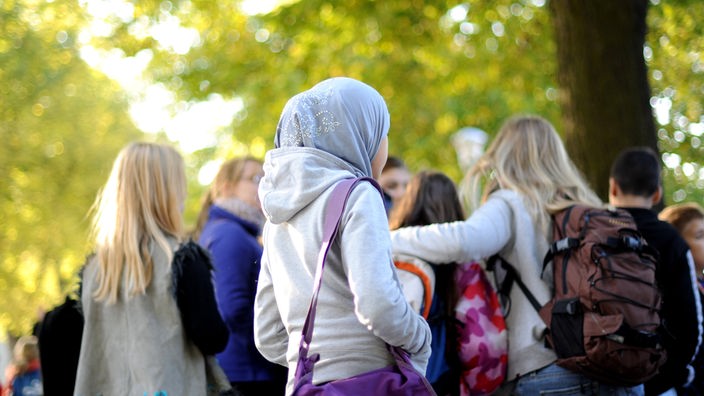  Ein Kind mit Kopftuch steht am Rand einer Schülergruppe