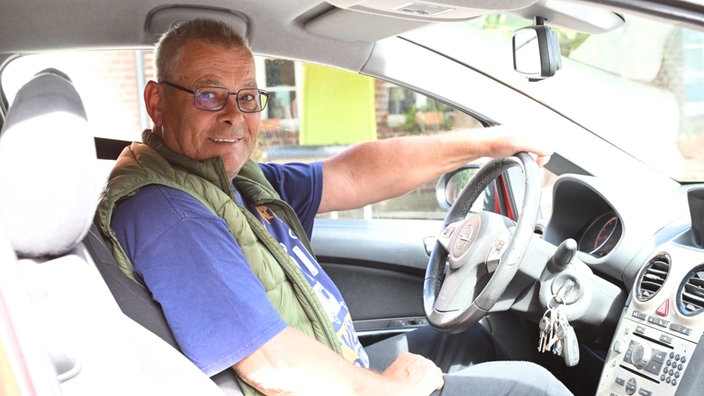 Ein Mann sitzt in einem Auto mit der linken Hand auf dem Lenkrad