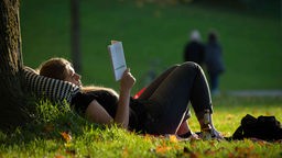 Frau liegt im Bürgerpark in Bielefeld (Nordrhein-Westfalen) und liest bei warmen Herbstwetter