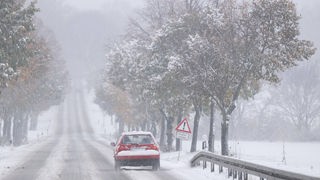 Ein roter PKW fährt über eine verschneite Landstraße