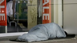 Ein Obdachloser schläft vor einem Geschäft in Köln.