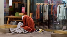 Ein Mann sitzt in der Innenstadt in einem Schlafsack im Eingang zu einem Geschäft. 