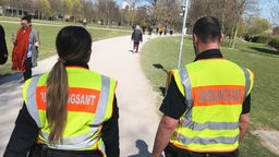 Zwei Mitarbeiter des Kölner Ordnungsamts von hinten, beim Kontrollgang durch den Grüngürtel