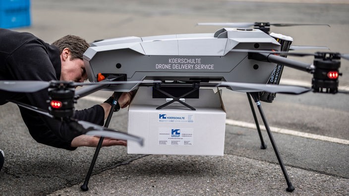 Ein Techniker befestigt das zu liefernde Paket an einer Drohne.