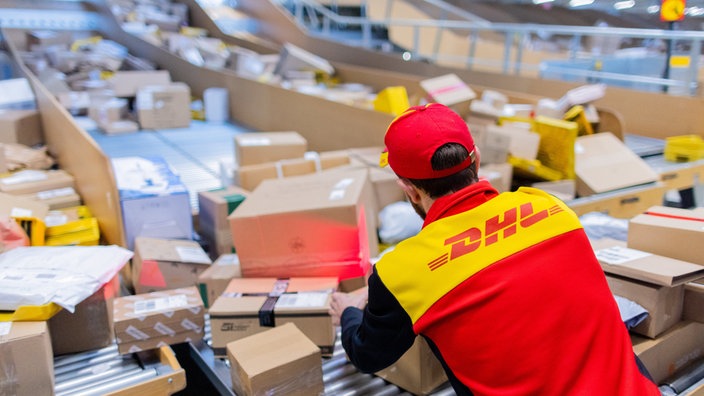  Ein Paketzusteller sortiert und räumt in einer Zustellbasis von DHL Pakete in ein Zustellfahrzeug.