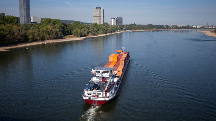 Ein Frachtschiff fährt auf dem Rhein bei Bonn, links ist der Posttower und der Lange Eugen zu sehen. 