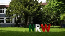 ie Buchstaben «NRW» stehen in den Landesfarben von Nordrhein-Westfalen vor der Zentralverwaltung der Hochschule für Polizei und öffentliche Verwaltung Nordrhein-Westfalen auf dem Rasen