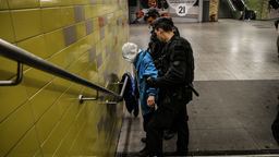 Zwei Polizisten kontrollieren an einer U-Bahnstation einen Mann mit Kapuze über dem Kopf