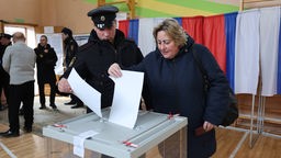 Mann und Frau werden Stimmzettel in eine Wahlurne