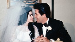 Das Paar Elvis Presley und Priscilla Beaulieu im Hochzeitsoutfit am Tisch.