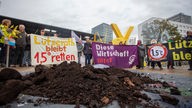 Mehrere Demonstrierende stehen vor einem verschüttetem Haufen Braunkohle. Sie tragen Banner mit den Aufschriften "Lützerath bleibt 1,5 Grad retten" oder "Diese Wirtschaft tötet"