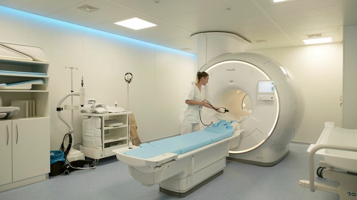 Eine Ärztin steht in einem hell erleuchteten Raum neben einm neuen MRT-Gerät