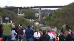 Zahlreiche Zuschauer verfolgen die Sprengung der Talbrücke von einer Wiese auf einem Berg in der Nähe.