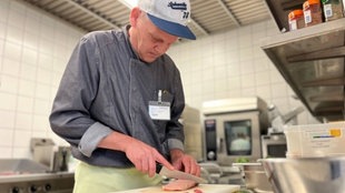 Mann mit Kappe und Messer in der Hand schneidet Fleisch