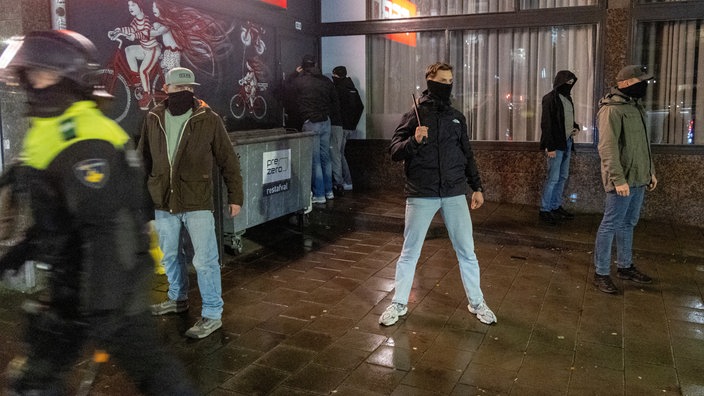 Vermummte Zivilpolizisten stehen bei Nacht vor einer Hausfassade in Amsterdam.