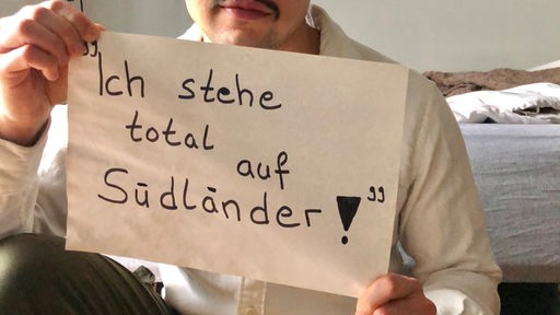 Lehramtsstudent Volkan Turan hält ein Schild hoch mit der Aufschrift: "Ich stehe total auf Südländer."