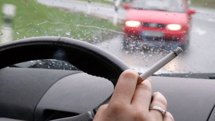 Eine Autofahrerin raucht bei regnerischem Wetter am Steuer ihres Fahrzeugs