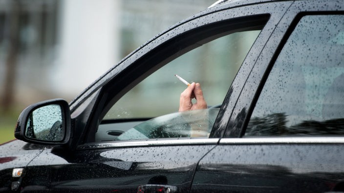 Ein Autofahrer raucht bei regnerischem Wetter am Steuer seines Fahrzeugs 