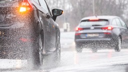 Ein Auto wirbelt Regenwasser auf, als es bei Dauerregen über eine Straße fährt.