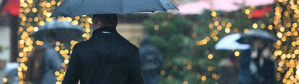 Mann mit Regenschirm läuft an Weihnachtsmarkt entlang