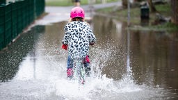Kind fährt durch große Regenpfütze