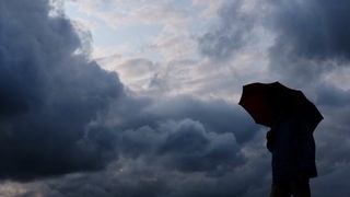 Ein Mann geht mit einem Regenschirm vor aufziehenden dunklen Wolken spazieren.