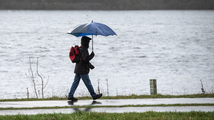 Ein Spaziergänger mit einem Regenschirm geht am Ufer des Kemnader Sees entlang