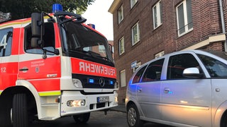 Ein Feuerwehrwagen und ein Auto stehen in einer engen Straße