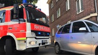 Ein Feuerwehrwagen und ein Auto stehen in einer engen Straße